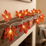Autumn maple leaf string lights glowing with warm orange and red lights, draped over a rustic wooden mantel in a cozy indoor setting.