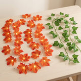 Orange autumn maple leaf string lights with warm glowing bulbs, displayed next to a green ivy garland on a light wood tabletop.