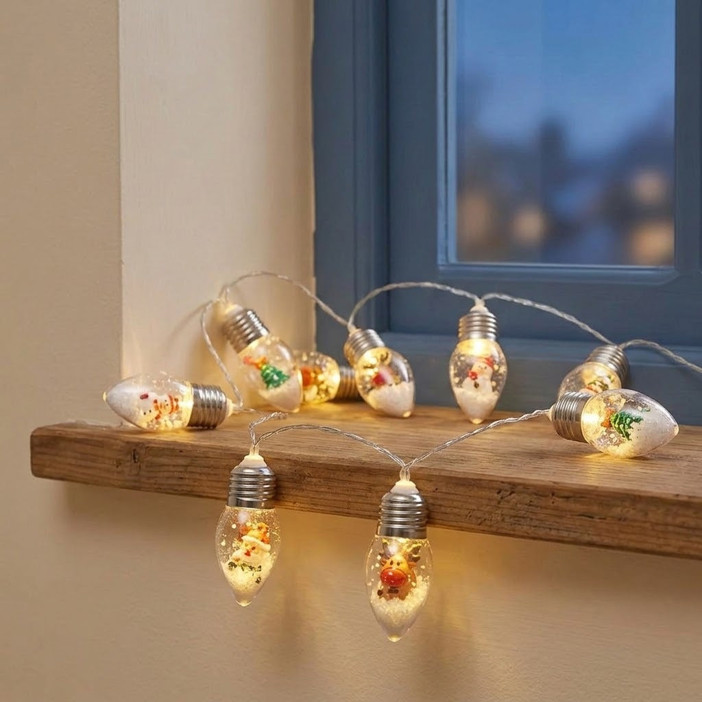 Warm white LED window string lights shaped like glass bulb filaments, decorated with dried flowers and glitter, draped over a wooden shelf next to a window.
