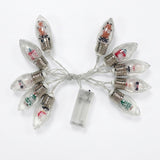 A set of clear C9 Christmas bulb string lights with silver screw bases, filled with decorative glitter and small holiday illustrations, connected by a clear wire to a transparent battery pack on a white background.