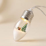 Christmas string lights feature a clear, silver-capped bulb containing a miniature green tree and gift, shown close up against a cream background.