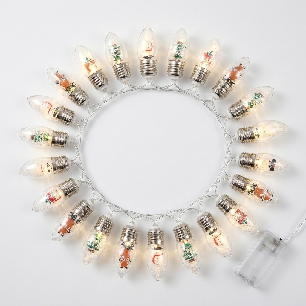 Christmas string lights with clear, silver-capped bulbs and miniature festive figures glow in a circle on a white background beside a battery box.