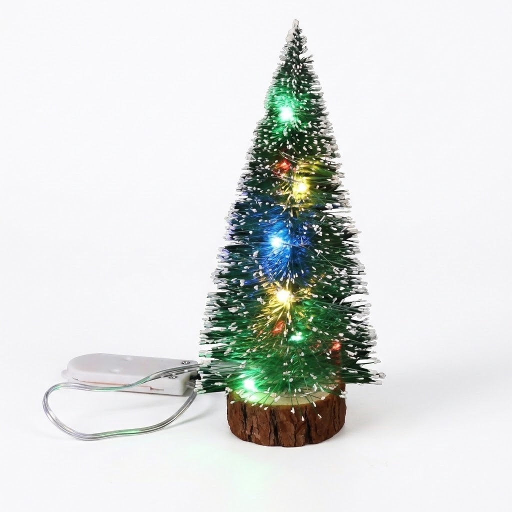 A green mini Christmas tree with white frosting, multicolor LED lights, a wooden-look base, and an attached white battery pack against white.