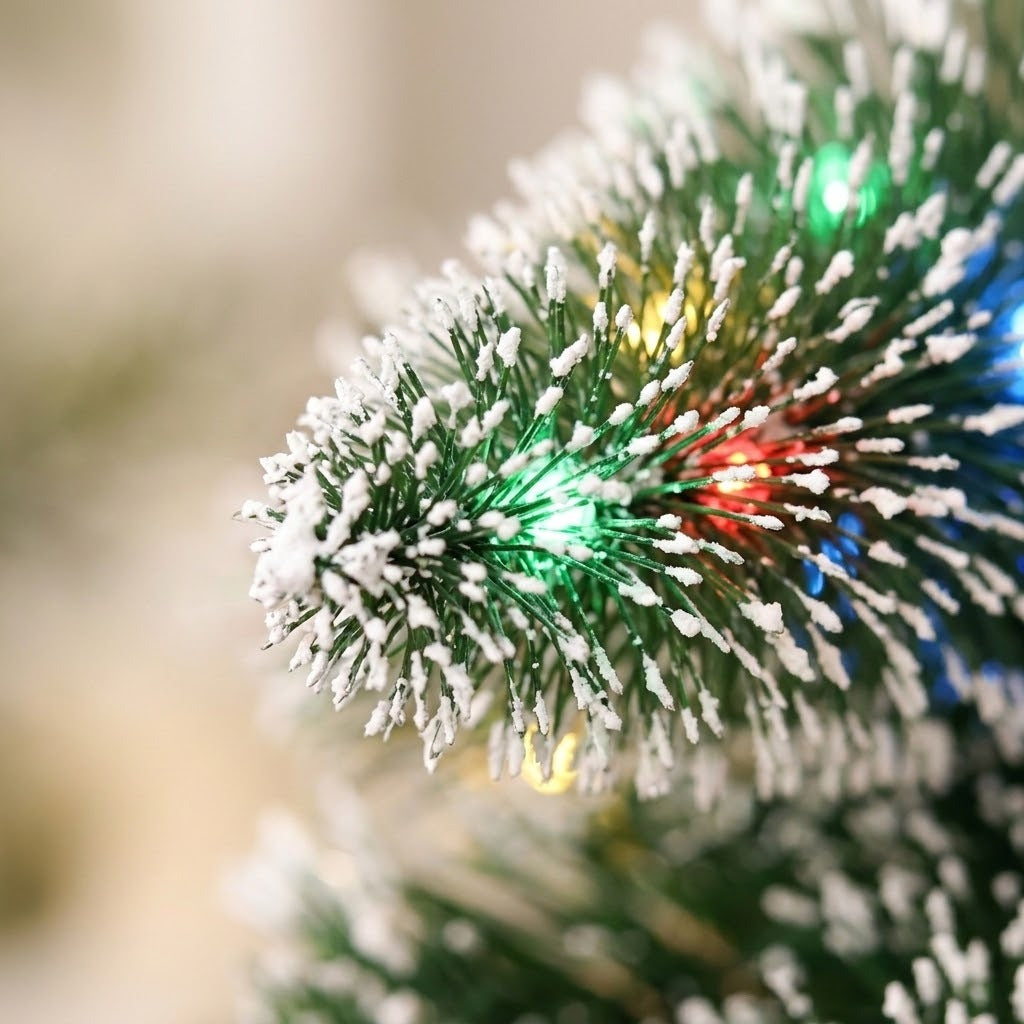 A close-up of the mini Christmas tree shows green artificial needles with white snow frosting and glowing multicolor LED lights.