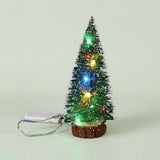 A snow-frosted green mini Christmas tree with multicolor lights stands on a wood base beside a white battery pack against a pale green background.