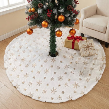 A round white faux-fur Christmas tree skirt with embroidered gold snowflakes, shown under a decorated Christmas tree on a light wood floor next to a beige armchair and wrapped gifts.