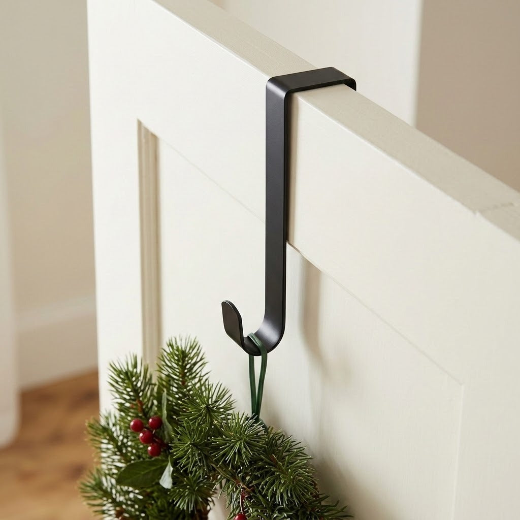 A black wreath hanger hooks over a white door, supporting evergreen foliage and red berries from a narrow green loop.