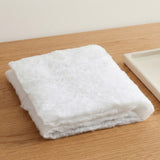 A white snow blanket is folded into layers on a light wood tabletop beside a partially visible cream tray.