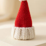 A small knitted Santa hat with a red pointed top and a white ribbed brim, photographed on a soft cream background.
