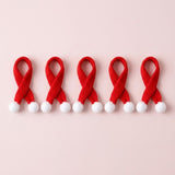 Miniature Christmas accessories include five red knitted scarves with crossed ends and white pom-poms arranged side by side on pale pink.