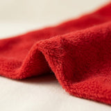 A close-up shows the red gift sack's fleece fabric folded on a light beige surface, revealing its fuzzy texture.