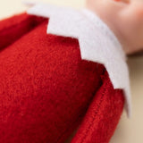 A close-up shows the elf doll’s fuzzy red fabric torso and arm beneath a white zigzag collar.