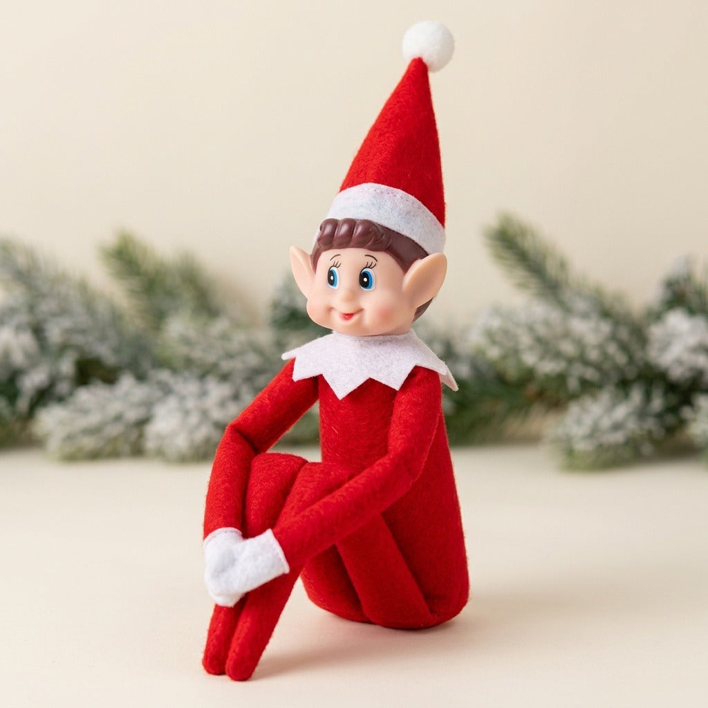 A red elf doll sits hugging its bent knees on a cream surface with frosted evergreen branches behind it.