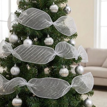 Silver mesh decorative ribbon forms wide gathered loops around a green Christmas tree with silver baubles beside a beige sofa.
