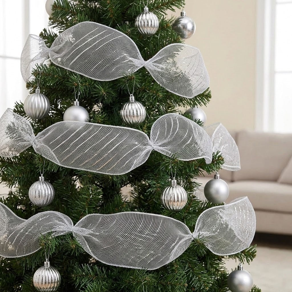 Silver mesh decorative ribbon forms wide gathered loops around a green Christmas tree with silver baubles beside a beige sofa.