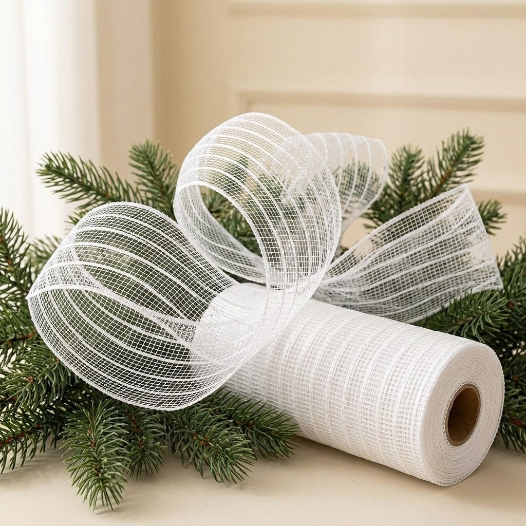 White striped mesh decorative ribbon forms large loops beside its roll among evergreen branches on a cream tabletop.