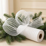 White striped mesh decorative ribbon forms large loops beside its roll among evergreen branches on a cream tabletop.