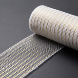 White mesh decorative ribbon with thin gold stripes extends from a roll across a dark grey surface.