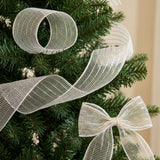 White mesh decorative ribbon forms a circular loop, flowing curves, and a bow on green Christmas tree branches.