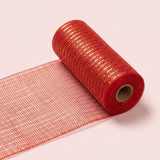 Red mesh decorative ribbon with shiny gold stripes lies partially unrolled diagonally on a pale pink background, with its cardboard core visible.