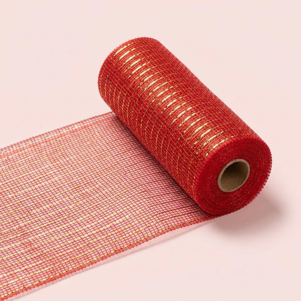 Red mesh decorative ribbon with shiny gold stripes lies partially unrolled diagonally on a pale pink background, with its cardboard core visible.
