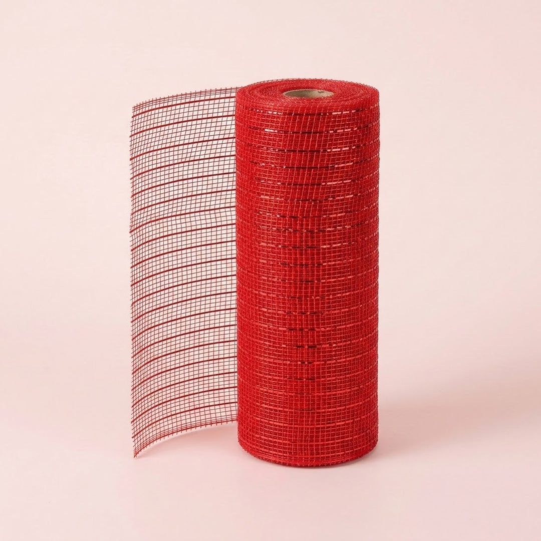 Red mesh decorative ribbon stands in an upright roll with a loose section extending left against a pale pink background.
