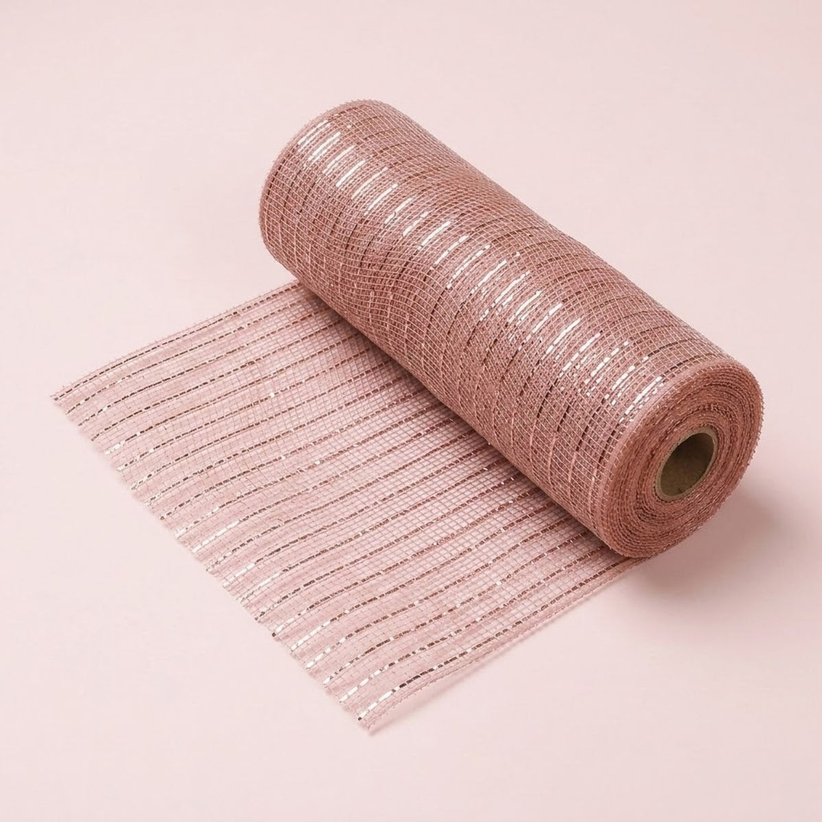Rose gold decorative ribbon with shiny stripes and an open mesh texture lies partially unrolled on a pale pink background.