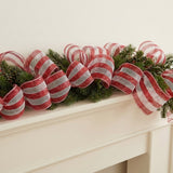 Red and white striped mesh decorative ribbon forms loops through an evergreen garland on a cream fireplace mantel.