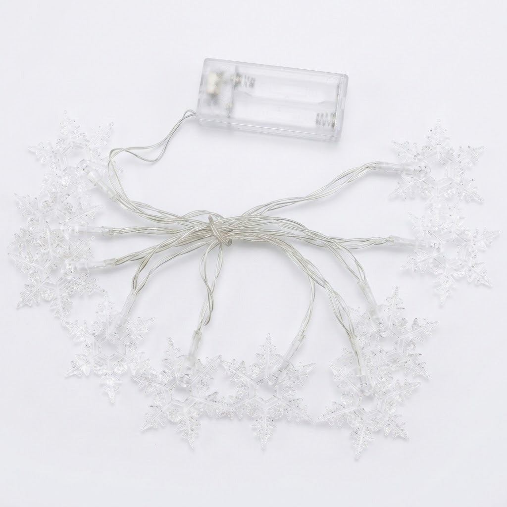 Unlit clear snowflake string lights with silver wire and an empty transparent battery box lie against a white background.