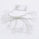 Unlit clear snowflake string lights with silver wire and an empty transparent battery box lie against a white background.