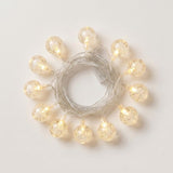 Textured clear globe string lights glow warm white around coiled silver-colored wire on a white background.