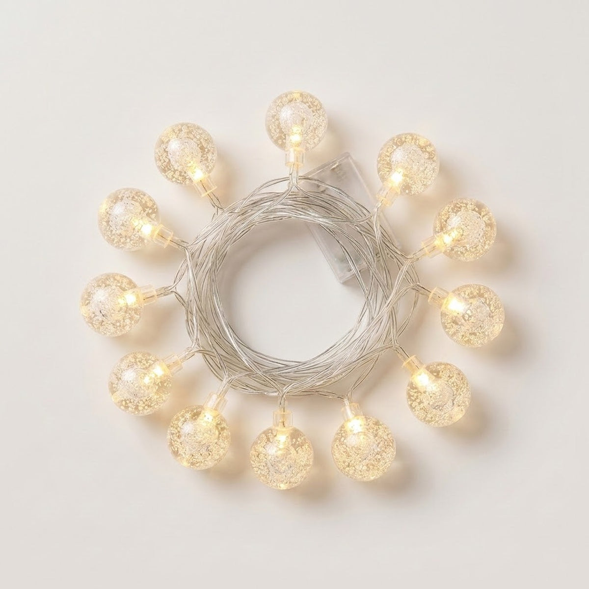 Textured clear globe string lights glow warm white around coiled silver-colored wire on a white background.