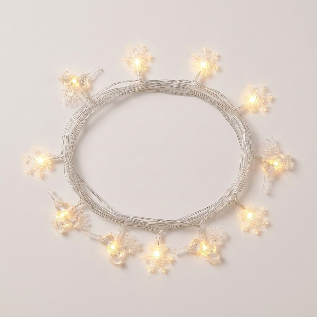 Clear reindeer and snowflake string lights glow warm white around a coil of silver-colored wire on a white background.