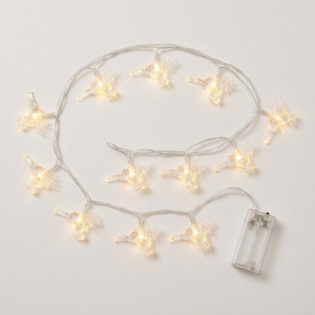 Clear reindeer-shaped string lights glow warm white on an off-white background, with silver-colored wires and a transparent battery box.