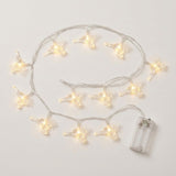 Clear reindeer-shaped string lights glow warm white on an off-white background, with silver-colored wires and a transparent battery box.