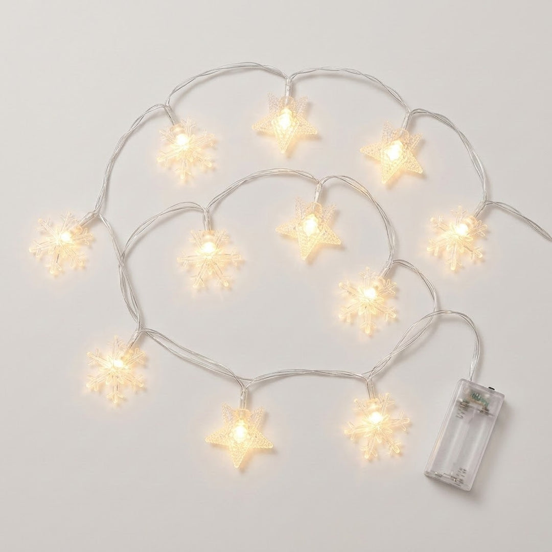 Clear star and snowflake string lights glow warm white along looping silver-colored wires beside a transparent battery box on white.