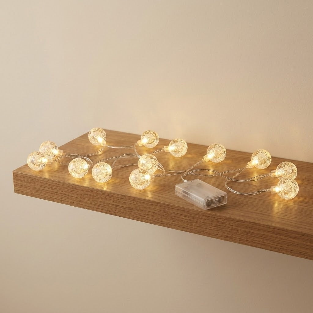 Clear bubble globe string lights glow warm yellow on a floating wooden shelf beside a transparent battery box.
