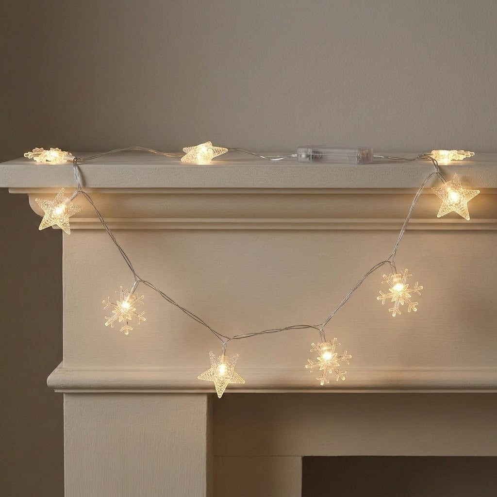 Clear star and snowflake string lights glow warm yellow across a white fireplace mantel, with a transparent battery box on top.