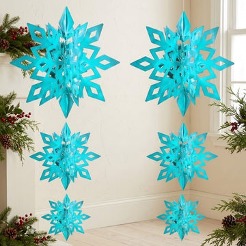 Six turquoise 3D snowflake ornaments hang in two columns beside a window, framed by evergreen branches, pinecones, and red berries.