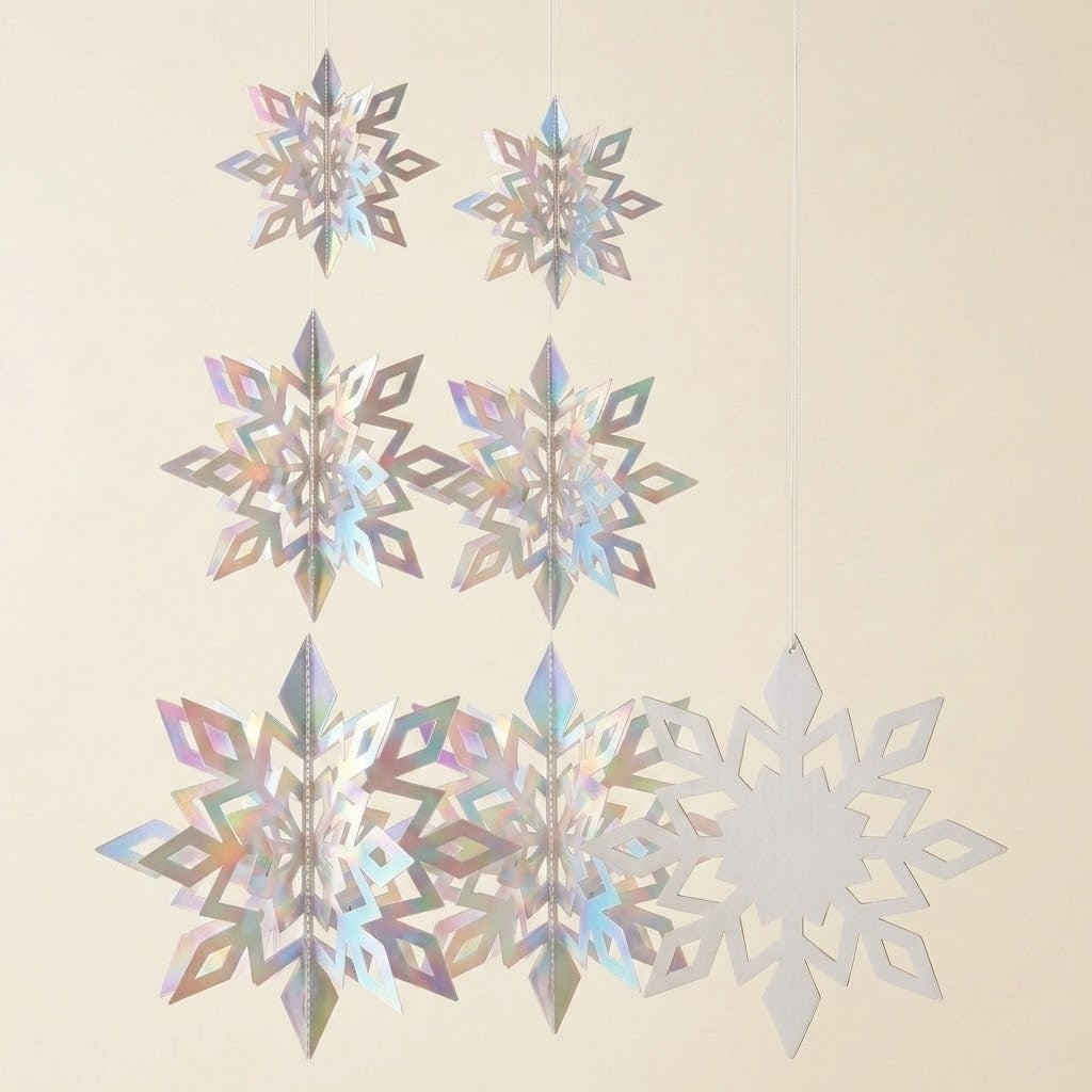 Iridescent silver snowflake ornaments hang against a cream background, showing six folded 3D shapes beside one flat snowflake.