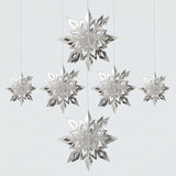 Six reflective silver 3D snowflake ornaments in three sizes hang at staggered heights against a light gray background.