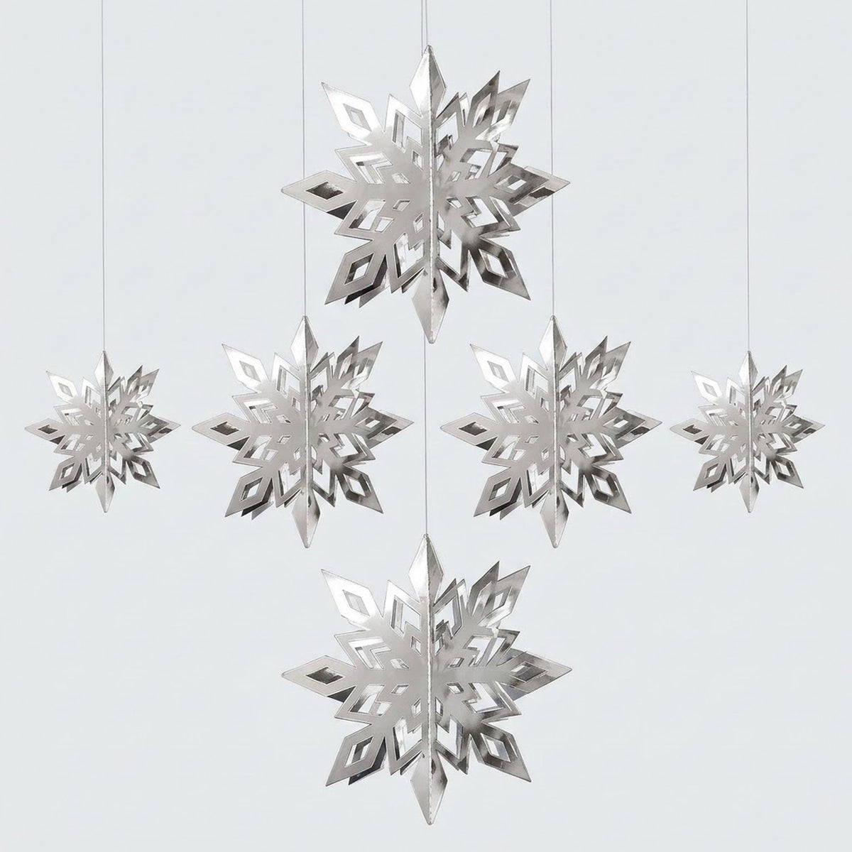 Six reflective silver 3D snowflake ornaments in three sizes hang at staggered heights against a light gray background.