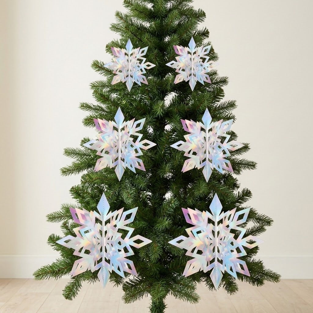 Six iridescent silver 3D snowflake ornaments hang in pairs on a green Christmas tree against a cream wall.