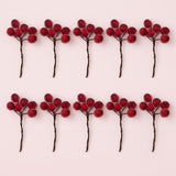 Ten artificial red berry picks with twisted brown stems are arranged in two rows of five on a pale pink background.
