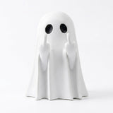 A white ghost figurine with black circular eyes and raised middle fingers, photographed against a seamless white background.