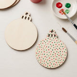 Wood ornament blanks, one unpainted and one decorated with red and green dots, lie beside brushes and paint on a white tabletop.