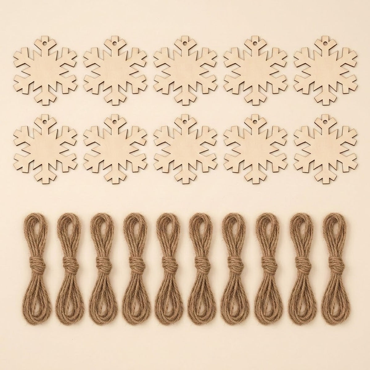 Ten unfinished wood snowflake ornament blanks with hanging holes sit above ten brown twine bundles on a cream background.