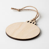 A round wooden ornament blank with a natural light wood finish, featuring a dark brown edge, a pre-drilled hole for a hanging string, and three small cutouts at the top. The ornament is suspended by a knotted piece of natural jute twine against a clean, light gray background.