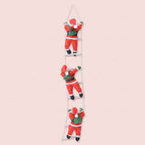 Three hanging Christmas decorations shaped like Santa Claus climbing a ladder, shown against a solid pale pink background.