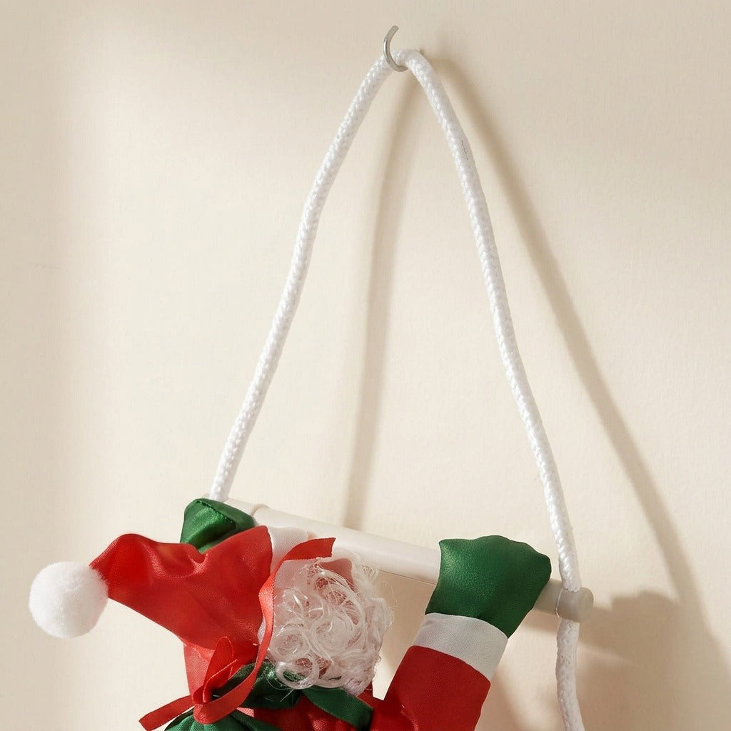 Close-up of the hanging Christmas decoration shows its white cord loop on a wall hook above Santa’s red hat and green mittens.